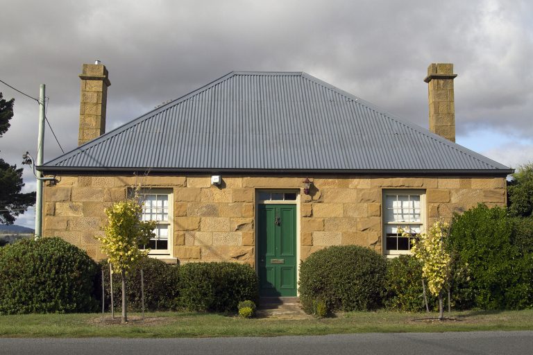 A sandstone house with a green front door, bathed in gorgeous light. Discover small towns in Tasmania worth visiting.