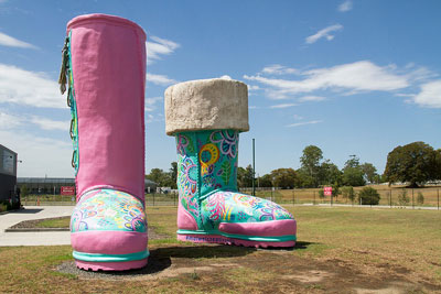 A woman with a brightly coloured t-shirt stands in front of two equally brightly coloured ugg boots. The boots are one of the big things in Australia and can be found in Thornton, New South Wales.