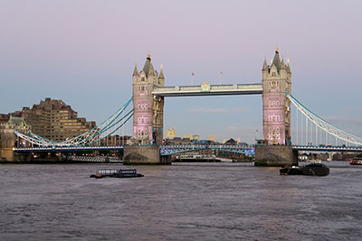 Tower Bridge in London around sunset. The bridge's lights are lit and a pastel blue and purple background sits behind it. Discover the best ways of travelling between London and Paris.
